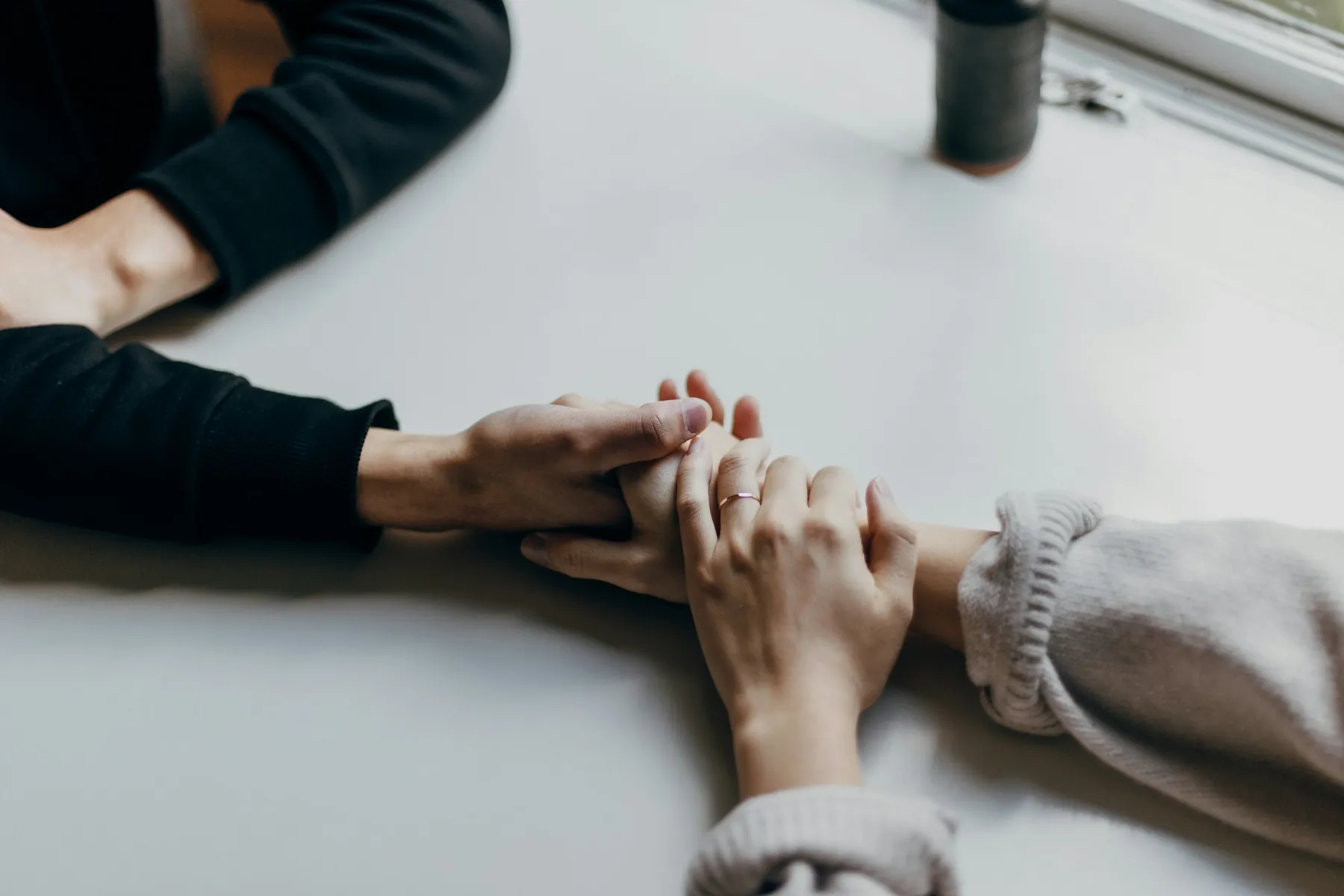 Two people holding hands across a table in support