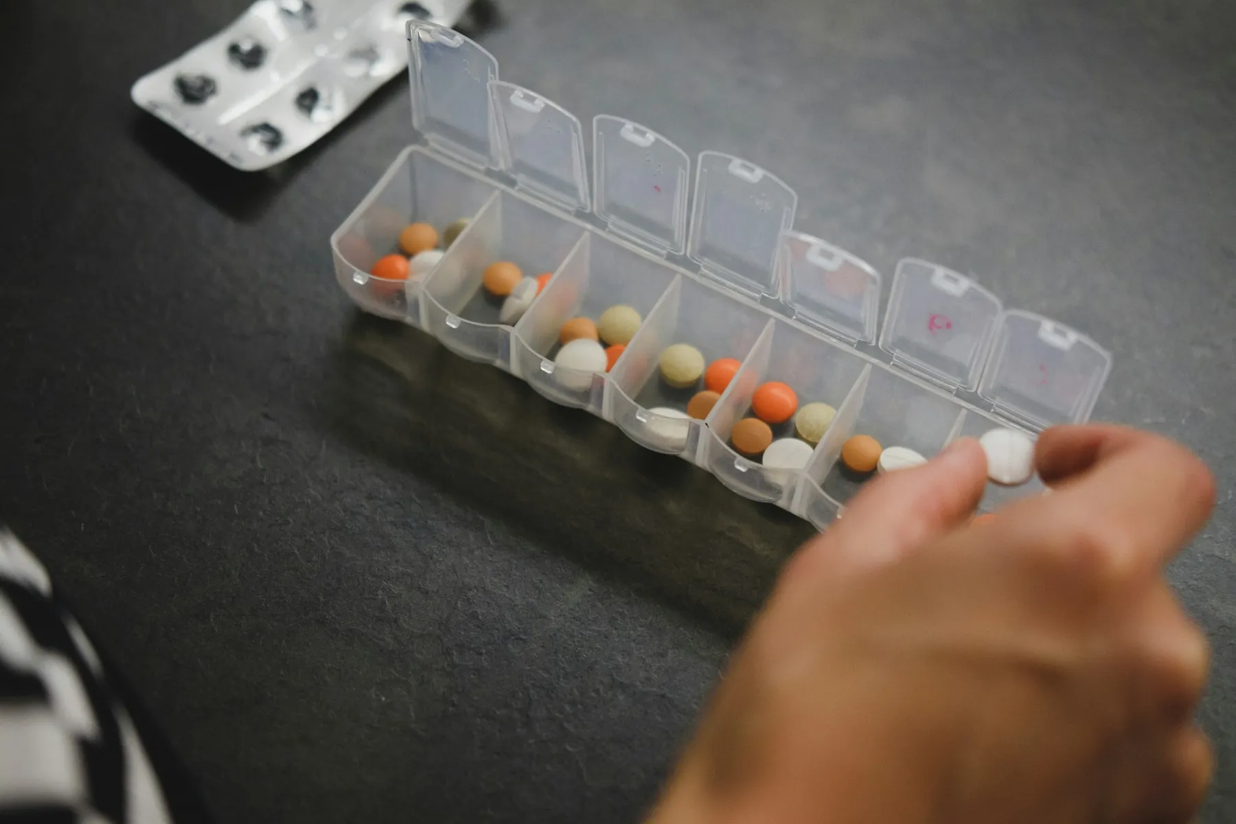 A hand reaching into a weekly pill organizer